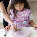 Toddler wearing a lavender Bumkins bib with unicorns, drawing with a marker on a clear suction plate.