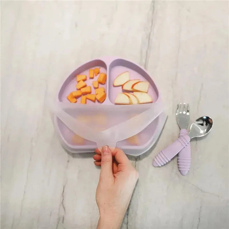 Bumkins lavender suction plate with three sections, filled with diced fruits, and a hand lifting a silicone cover.