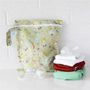 Waterproof Bumkins wet bag with camping-themed design beside stacked clothes and containers.