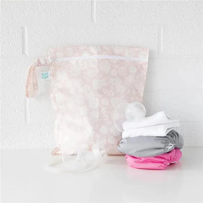 Bumkins wet bag in floral pattern, with pink, gray, and white baby items stacked beside it.
