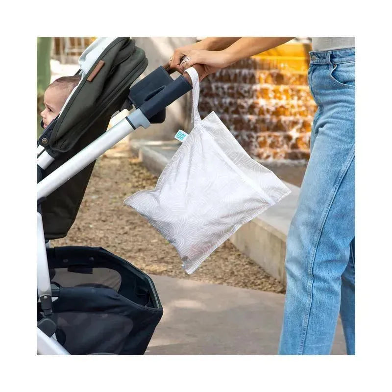 Bumkins Wet Bag in a light pattern is being held by a person beside a stroller with a baby inside.