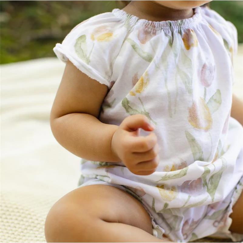 A child sits with a folded arm, wearing a white bubble romper decorated with colorful tulip prints.