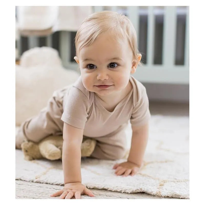 Baby crawling on a light rug, wearing a pink sand-colored short sleeve bodysuit, smiling at the camera.