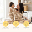 A mother and her baby, both wearing beige striped pajamas, share a joyful moment in a cozy laundry room.