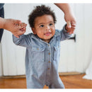 Infant wearing a light blue acid wash jumpsuit with two chest pockets, smiling while being held by an adult.