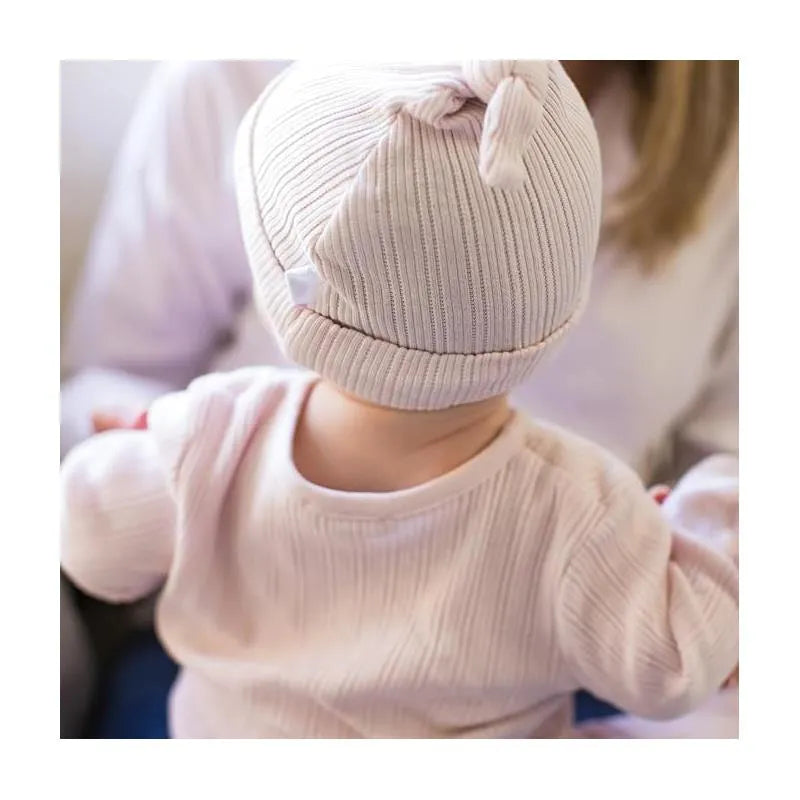 Baby wearing a soft lavender ribbed jumpsuit and matching hat, seen from behind, in a cozy setting.