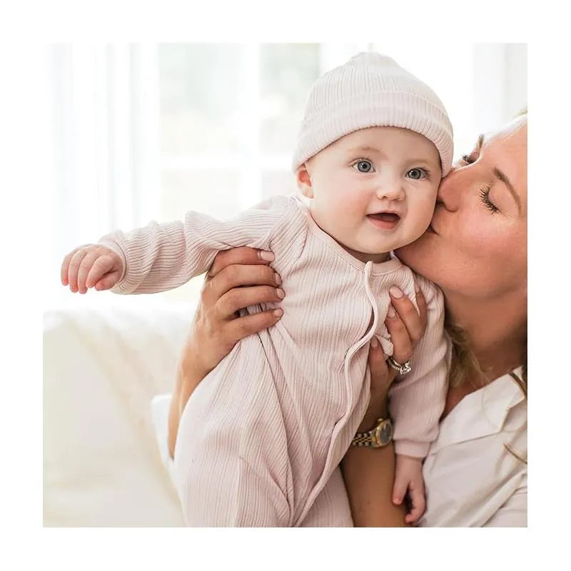 Baby girl wearing a sweet lavender ribbed jumpsuit and hat, held by an adult, smiling in a bright room.