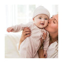 Baby girl wearing a sweet lavender ribbed jumpsuit and hat, held by an adult, smiling in a bright room.