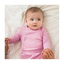 Baby girl wearing a pink ribbed wrap front bodysuit, lying on a white blanket, holding hands with an adult.