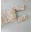 Baby wearing a beige Burts Bees Sleep & Play outfit with cloud patterns, on a light blue sheet with moon graphics.