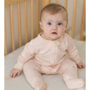 Infant sitting in a crib wearing a light pink, long-sleeve sleep and play outfit with a button closure.