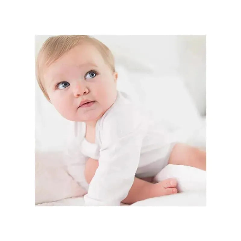 A baby in a white long sleeve bodysuit sits on a soft surface, looking curiously to the side.