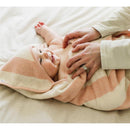 Baby wrapped in a striped pink and cream towel with a hood, smiling while being held by a caregiver.