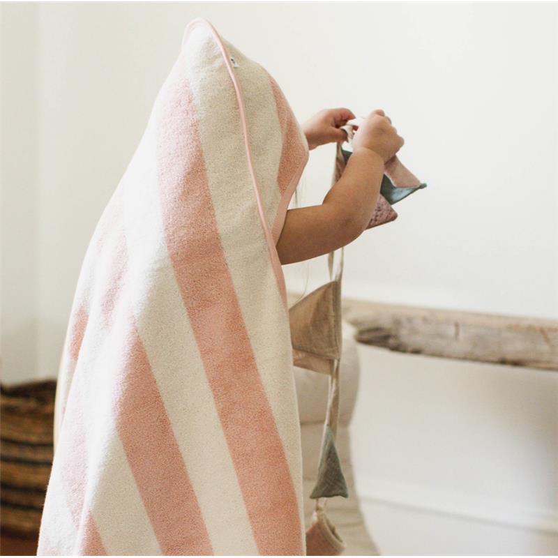 A child wearing a pink and cream striped towel plays with colorful fabric toy shapes in a bright, minimalist room.