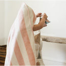 A child wearing a pink and cream striped towel plays with colorful fabric toy shapes in a bright, minimalist room.