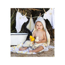 Toddler wearing a hooded towel, holding rubber ducks, with laundry hanging and a bowl nearby.