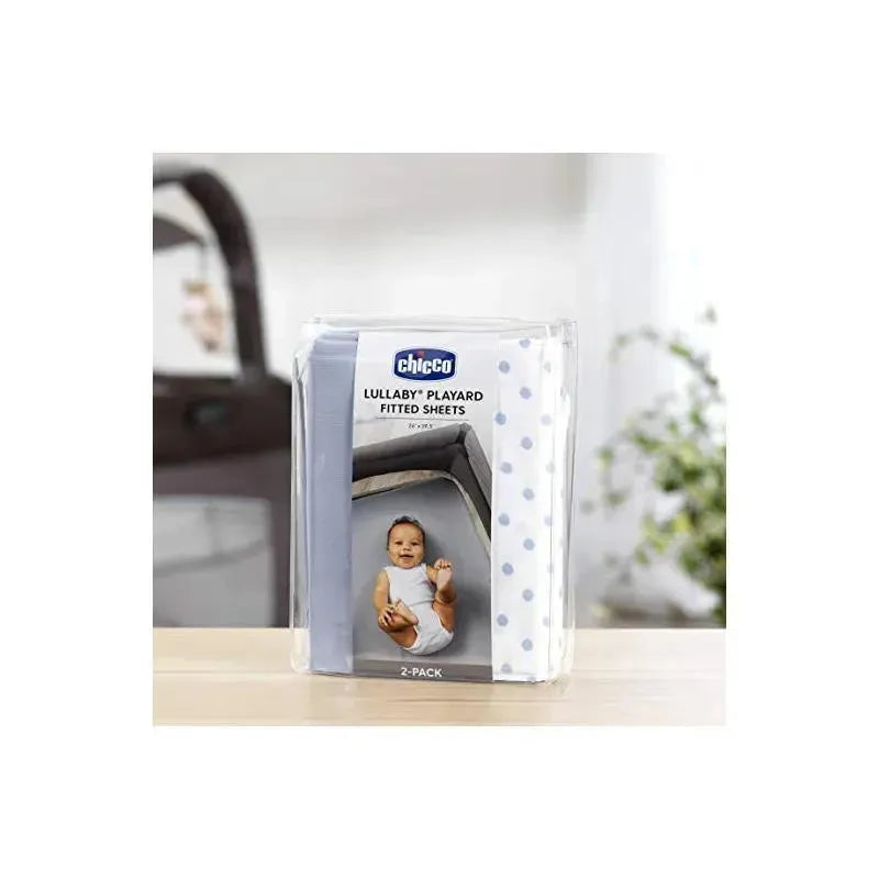 Chicco 2 Pack Lullaby Playard Sheets in blue dot pattern, featuring a baby on the packaging, displayed on a table.