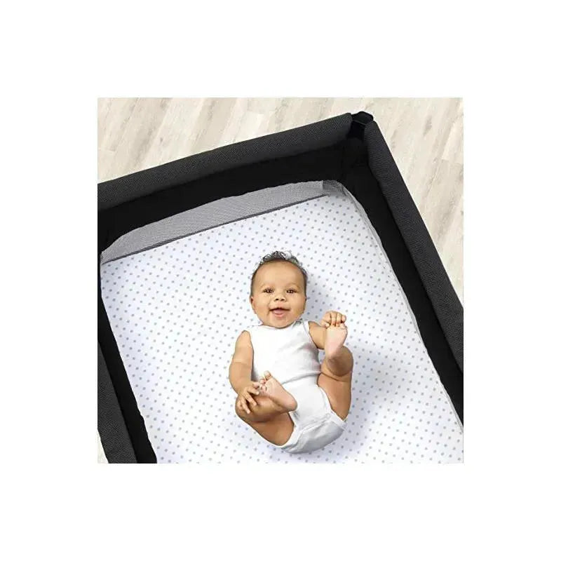 Chicco 2 Pack Lullaby Playard Sheets in blue dot design, featuring a baby smiling while lying on the sheet in a playard.