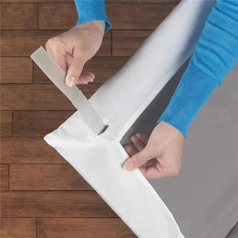 Hands adjusting a white Chicco playard sheet corner, showcasing its secure fit and soft material against a wooden floor.