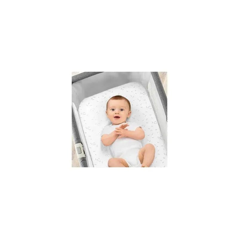 Grey triangle patterned bassinet sheet set featuring a baby in a white onesie, lying in a bassinet.