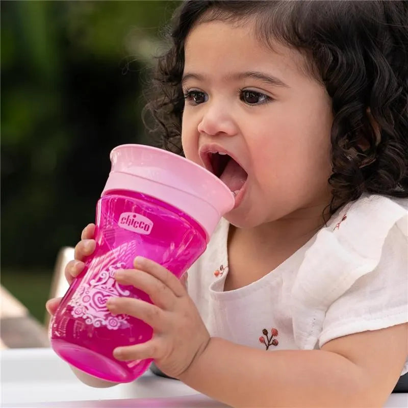 Chicco 360° Spoutless Rim Trainer Sippy Cup in pink, held by a toddler, who is preparing to drink from it.