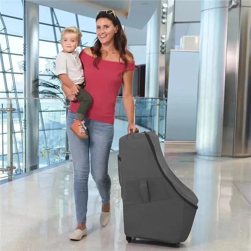 Woman carrying a child, holding a Chicco anthracite car seat travel bag with wheels in an airport setting.