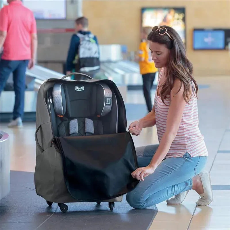 Chicco car seat travel bag in anthracite, with a woman kneeling and unzipping it at an airport baggage claim.