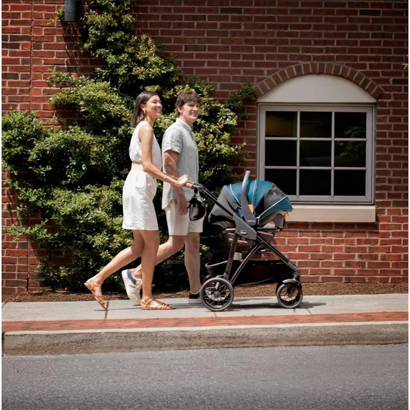 Couple walking with the Chicco Corso Primo ClearTex Modular Travel System stroller on a sunny sidewalk.