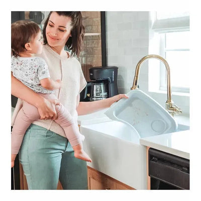 A woman holding a toddler smiles while washing a gray sink insert in a modern kitchen.