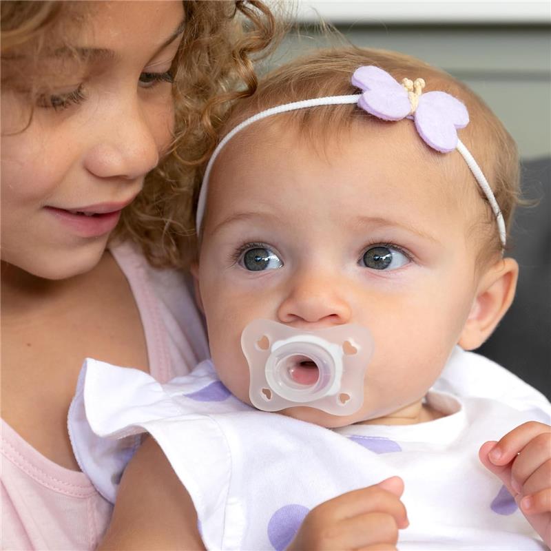 Child with a clear Chicco Physioforma Mini Orthodontic Pacifier, gazing at an older girl nearby.
