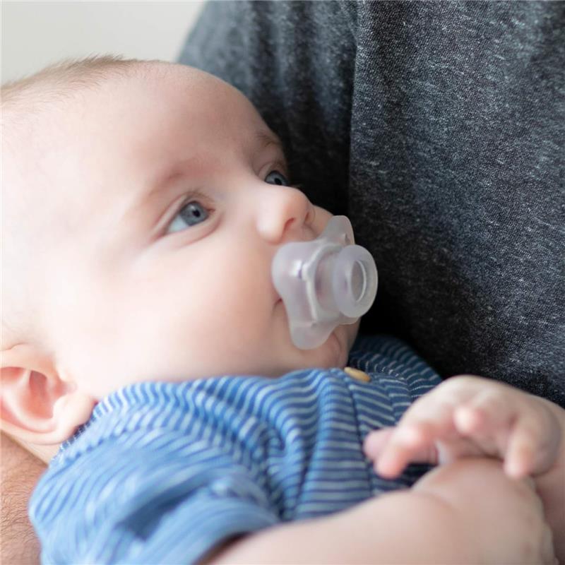 Baby with a clear orthodontic pacifier, wearing a blue striped shirt, being held closely.