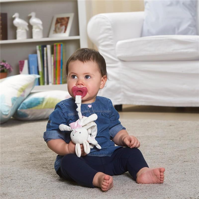 Baby girl sitting on a carpet, holding a pacifier and a soft toy, wearing a denim shirt and navy leggings.