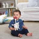 Baby girl sitting on a carpet, holding a pacifier and a soft toy, wearing a denim shirt and navy leggings.