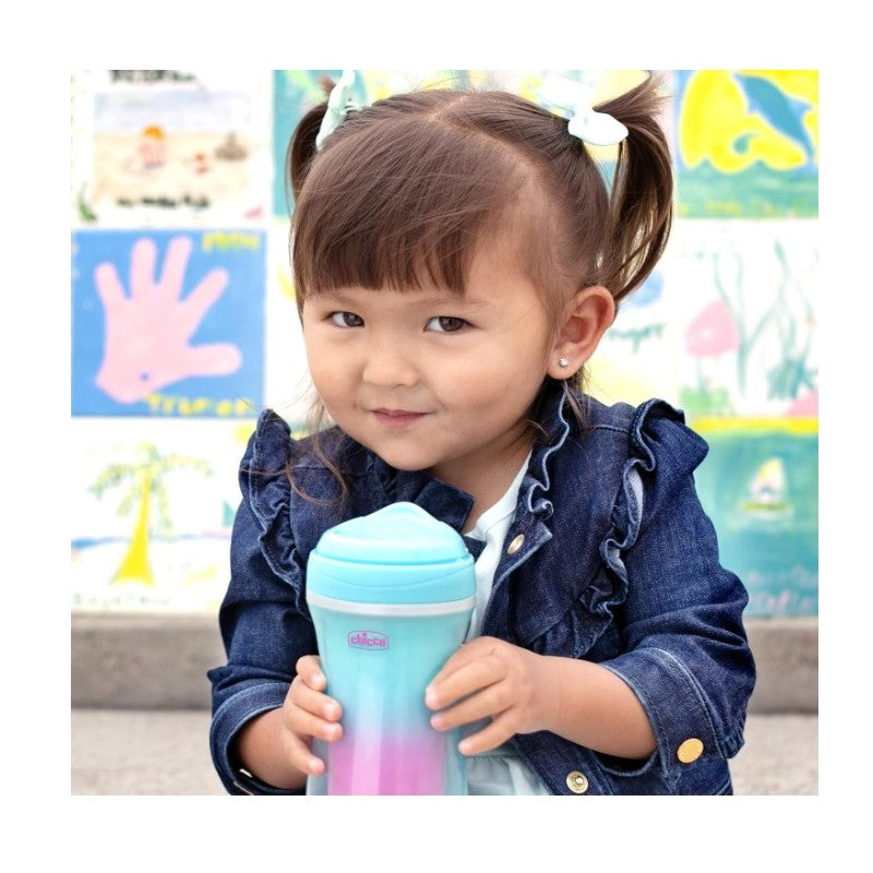 Chicco insulated rim spout trainer sippy cup in teal and pink held by a smiling child in front of colorful artwork.