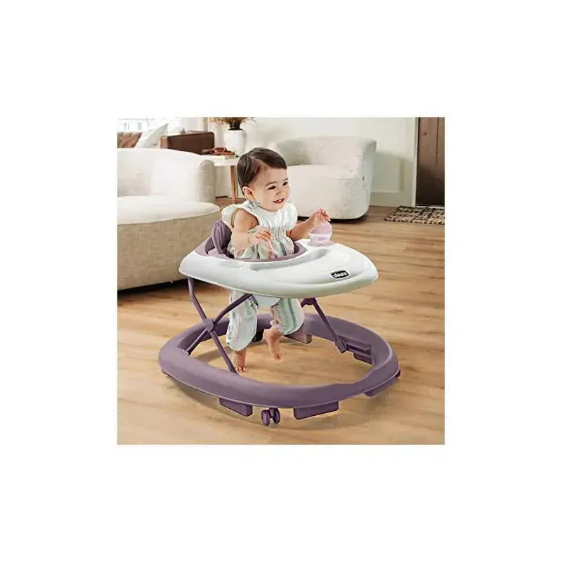 Infant girl in a lavender Chicco Mod Walker, smiling and reaching for a toy, with a cozy living room backdrop.