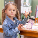 Child holding a Chicco My Tumbler open rim water bottle in pink, featuring a free-flow spout, set at a table.