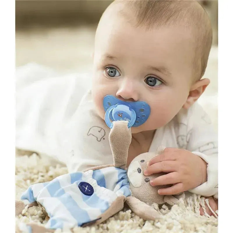 Baby with blue pacifier cuddles a Chicco Pocket Buddy plush toy, featuring a patterned outfit and soft textures.