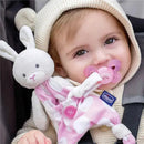 Baby in a cozy outfit with a bunny plush and a pink pacifier, contently smiling while seated.