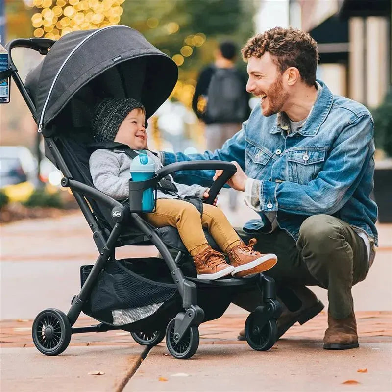 Chicco Presto self-folding compact stroller in graphite with a smiling child and a parent interacting outdoors.
