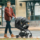 A man with glasses pushes a Chicco Presto self-folding compact stroller in graphite color while walking outdoors.