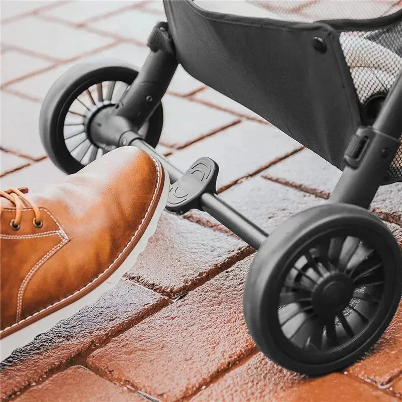 Foot pressing the folding mechanism of the Chicco Presto Self-Folding Compact Stroller, with graphite fabric and wheels visible.