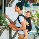 Mother using the Chicco Snugsupport 4-In-1 Infant Carrier in Black, holding a wallet while interacting with a building.