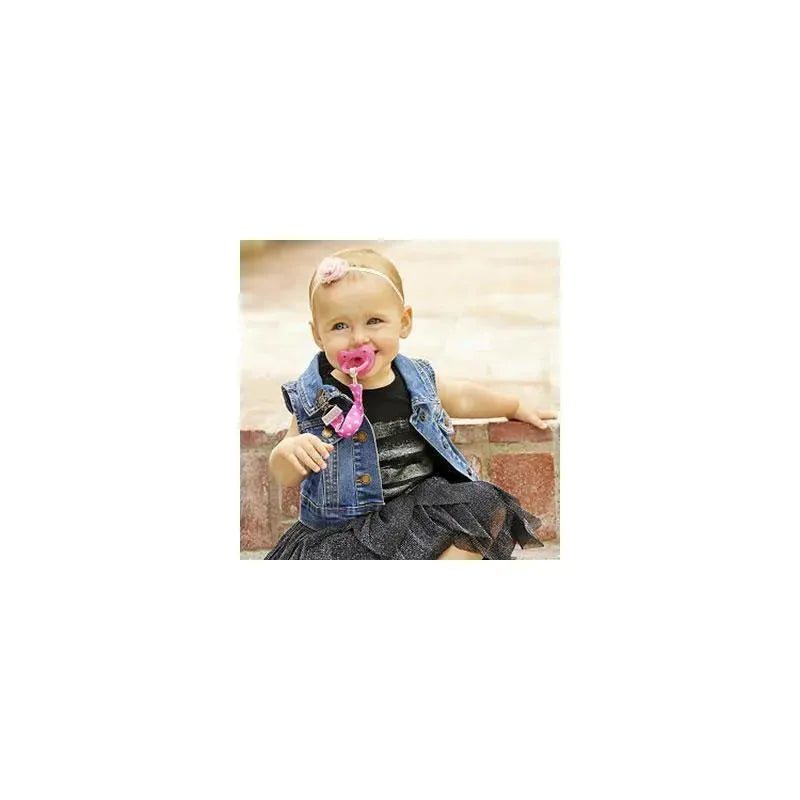 Toddler sitting on steps, wearing a denim vest and black dress, holding a pink pacifier attached to a grey clip.