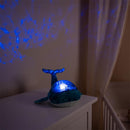 Blue Eco Tranquil Whale night light projecting calming blue patterns on the wall, sitting on a white dresser.