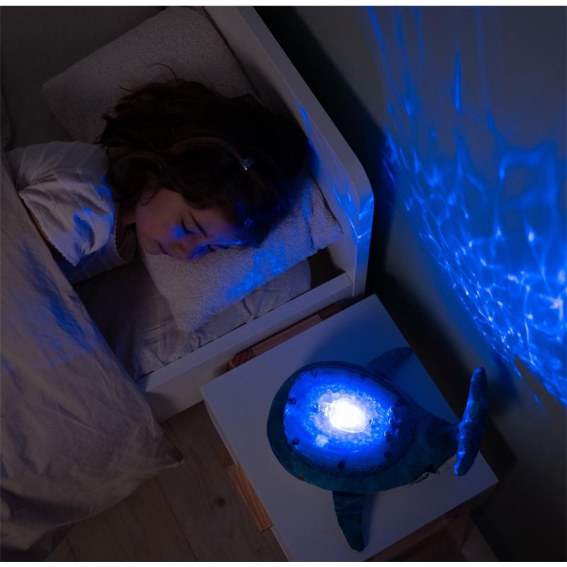 Blue Eco Tranquil Whale night light projects calming ocean waves onto the wall while a child sleeps beside it.