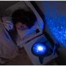 Blue Eco Tranquil Whale night light projects calming ocean waves onto the wall while a child sleeps beside it.