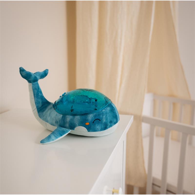 Blue Eco Tranquil Whale by Cloud B, a plush nightlight and sound machine, resting on a white surface near a crib.