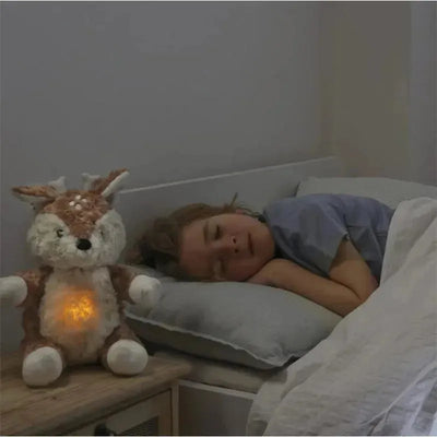 Finley Fawn, a plush nightlight, sits beside a sleeping child, glowing softly, creating a comforting bedtime atmosphere.