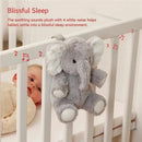 Gray plush elephant sound machine with musical notes, resting on a crib railing, next to a baby in a beige sweater.