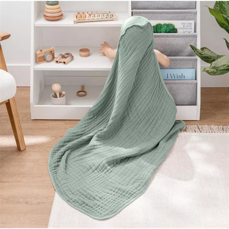 Hooded towel in fern color draped over a child sitting on the floor, surrounded by toys and a shelf of books.